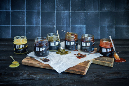 Captivating lifestyle shot of the full range of Killer Condiments artisanal sauces – open jars of Chimichurri, Blood Orange Hot Sauce, Sticky Soy, and Crispy Chilli Oil – tantalizingly dripping down the sides, with spoons lavishly coated in vibrant sauces, set against a minimalist background to accentuate the rich and alluring textures of these gourmet delights.